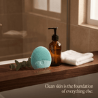 Teal cleansing device, brown bottle, and white towel on a wooden surface with a blurred bathroom background.