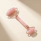 Pink facial roller with rose gold accents on a beige background