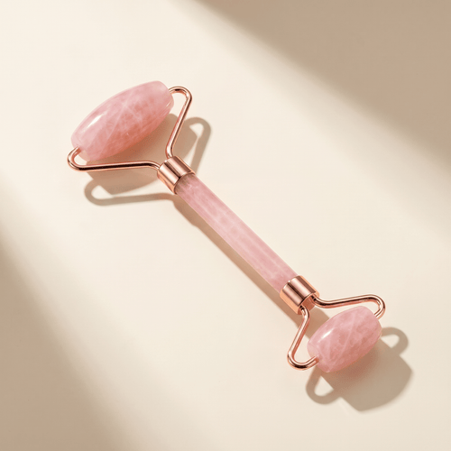 Pink facial roller with rose gold accents on a beige background