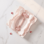 Rose gold facial roller on a marble surface with pink stones