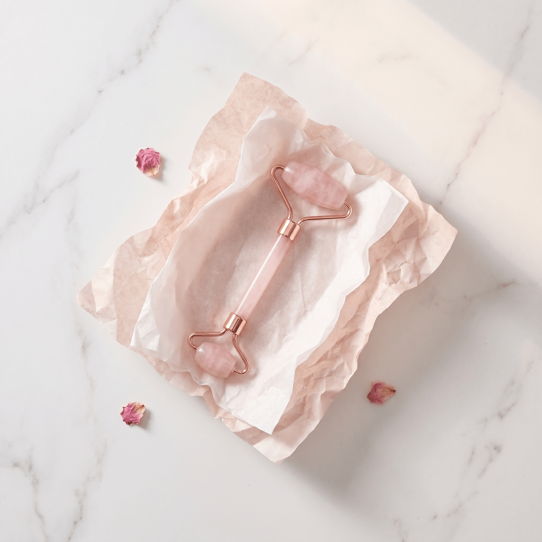 Rose gold facial roller on a marble surface with pink stones