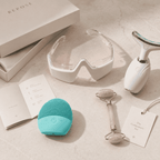 Collection of skincare and wellness tools including a teal device, goggles, and roller on a neutral background.