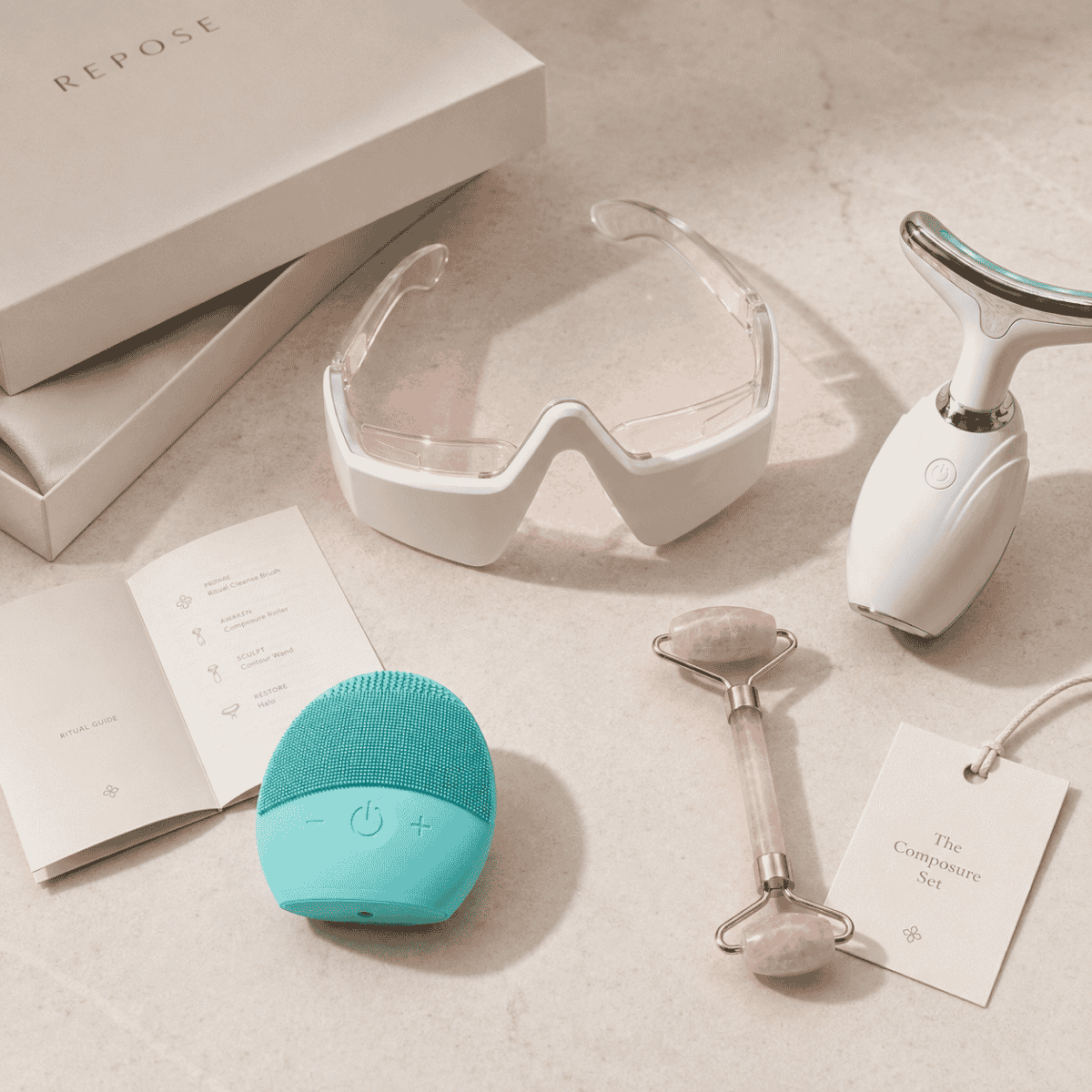 Collection of skincare and wellness tools including a teal device, goggles, and roller on a neutral background.